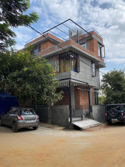 The exterior of Ramya and Madhu’s home, a contemporary structure that combines exposed brick with smooth grey concrete panels. The design includes a rooftop pergola, creating usable outdoor space on a city plot.