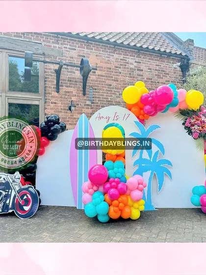 A vibrant beach-themed 17th birthday party. The setup includes surfboard cutouts, palm trees, and even a motorcycle prop for a cool, edgy vibe.
