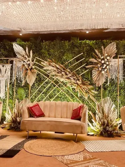 A full view of our nature-inspired boho stage for Anuja and Amit. The combination of a green wall, macrame, dried grasses, and natural fiber rugs creates a warm, earthy, and incredibly stylish setting.