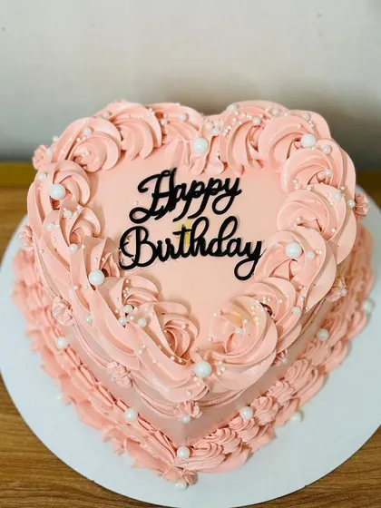 A classic heart-shaped birthday cake with beautiful pink frosting swirls.