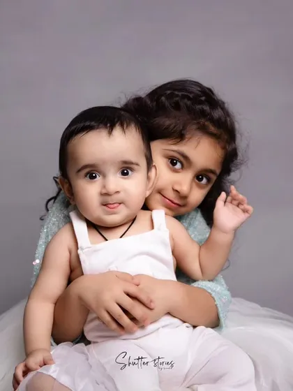 A sweet portrait of a sister holding her baby brother, both looking at the camera.