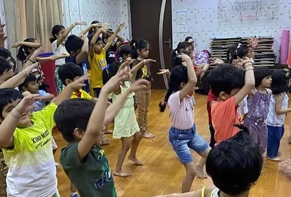 An instructor demonstrates a dance move to a class of young learners. This photo shows how our gurus lead by example, making it easy for kids to follow along and build confidence.