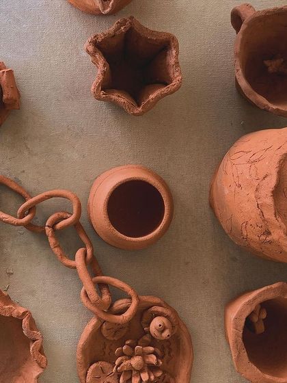 A collection of small, hand-built terracotta pieces, including a rose, a star-shaped pot, and a delicate chain. This is the result of a playful, experimental session with clay.