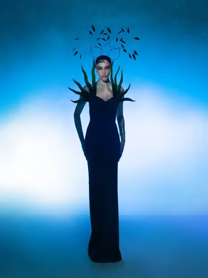 This variation of the conceptual look adds a feathered headpiece, further enhancing the avant-garde and surreal quality of the styling. The pose is deliberately statuesque.