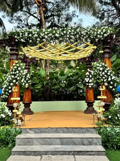 A full view of the peacock-themed mandap, with its traditional wooden pillars and lush white floral arrangements, creating a serene and elegant atmosphere.