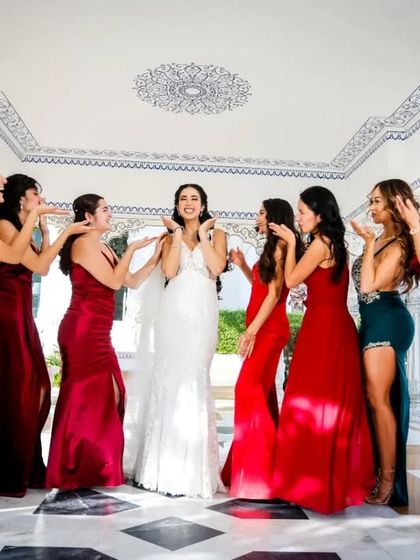 The bride in her white gown poses with her bridesmaids, who are all dressed in matching red dresses.