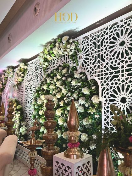 A side view of the white floral stage, highlighting the texture of the flower wall and the traditional brass elements placed alongside it.