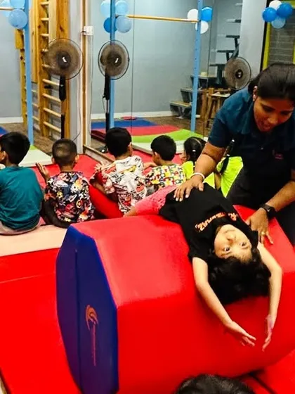 Safety and proper technique are at the core of our teaching. Here, an instructor provides hands-on support to a young gymnast learning a backbend over a soft octagonal tumbler, ensuring she builds flexibility and strength correctly.