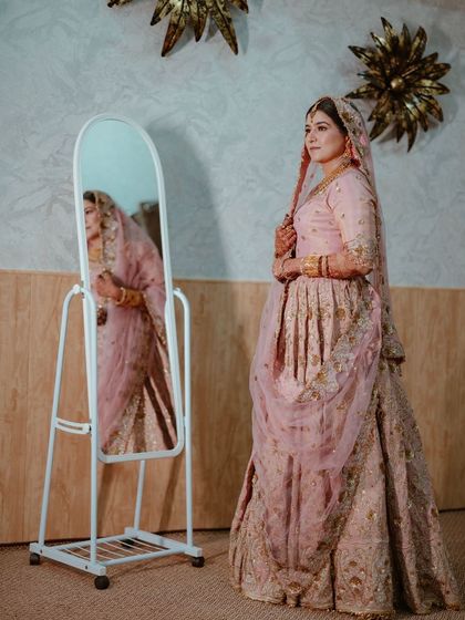 A full-length portrait of the bride in her elegant pink Nikkah outfit, her reflection adding a layer of depth to the image.