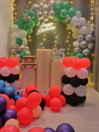 A 25th birthday celebration setup with green, silver, and white balloons. The light-up number "25" makes the milestone clear, and the floor is covered in colorful balloons.