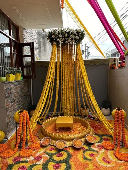 An intimate Haldi setup perfect for a home ceremony. We used a canopy of marigold garlands over a traditional brass urli, with a floor covered in a colorful flower rangoli.