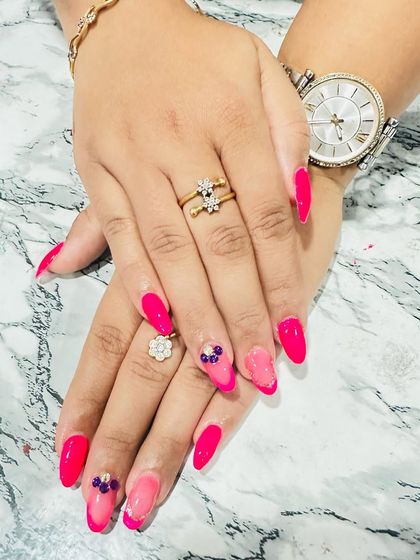 A vibrant hot pink set with a subtle French ombre on the accent nails, which are adorned with small, colorful rhinestone clusters.