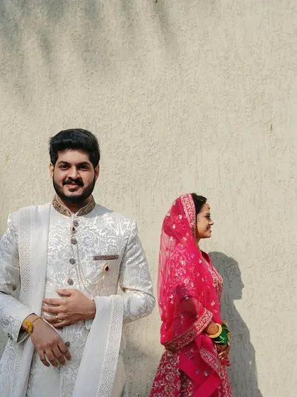 An artistic shot using shadows and light. The bride's vibrant pink veil contrasts beautifully with the groom's white sherwani, creating a modern and stylish portrait.
