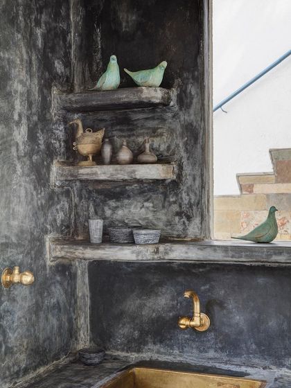 A detail of a bathroom nook, featuring a dark polished cement finish, brass fixtures, and handcrafted decor. Every corner of Jalakara is curated with objects and crafts from different parts of India.