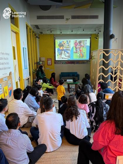 Parents and children watch a presentation showcasing their journey through the school year. These audiovisuals are a powerful way to document and celebrate the hands-on explorations and moments of curiosity.