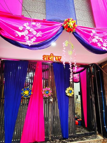 A striking entrance decoration using royal blue and bright pink drapes, accented with a 'Shaadi Ghar' sign and floral details.