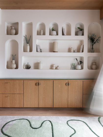 This custom-designed storage unit features a ribbed wood finish and is topped with a glass surface. Above it, a series of arched niches are carved into the wall for a beautiful, integrated display.