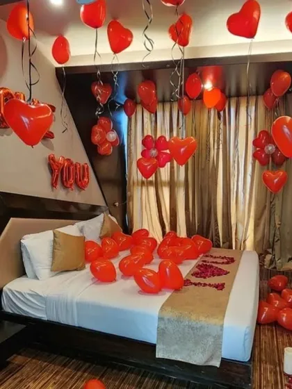 A hotel room filled with red heart-shaped balloons for a romantic occasion. The bed is decorated with 'I LOVE YOU' made from petals, creating a classic and heartfelt surprise.