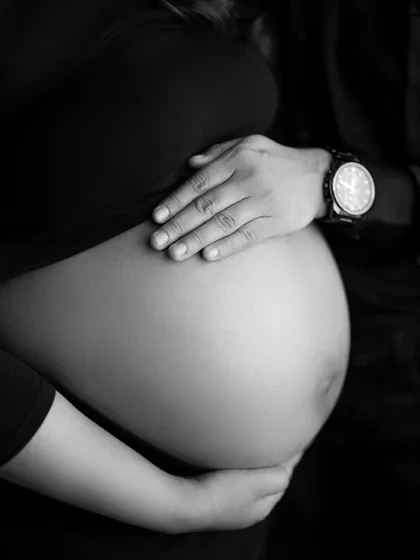 A close-up detail shot in black and white, focusing on their hands resting on the baby bump. A powerful symbol of new life and shared love.