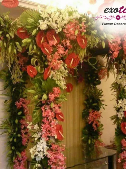 A lush and tropical floral arch. This entrance decoration is filled with red anthuriums, pink orchids, and dense greenery, ideal for a grand welcome during festive seasons.
