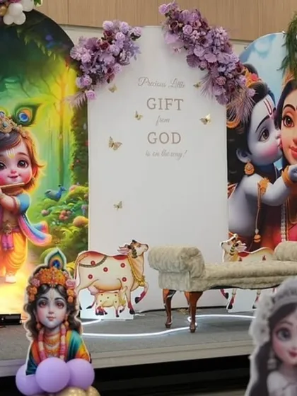 A beautiful baby shower stage in a purple and gold color scheme. The decor includes custom backdrops with Krishna illustrations, a sign that reads 'Precious Little Gift From God', and a small chaise lounge for the mother-to-be, all surrounded by purple and gold balloons.