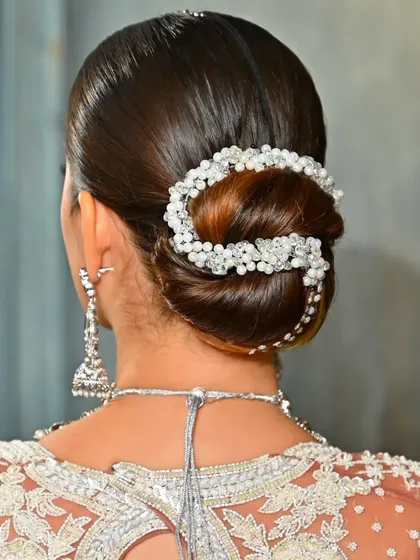A detailed back view of a polished low bun, elegantly wrapped with a pearl and crystal hair accessory. This style is perfect for a sophisticated bridal or evening wear shoot.
