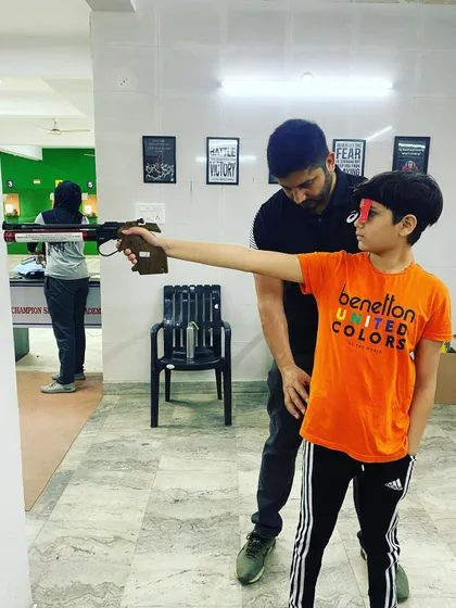 Guiding a young shooter as he practices his aim. Hands-on correction helps in developing muscle memory for the correct shooting posture.