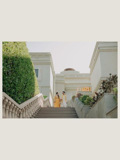 A wide shot of Mehul and Divya on the grand staircase of Raffles Udaipur during their Haldi. This image captures the scale of the venue and the elegance of the couple.