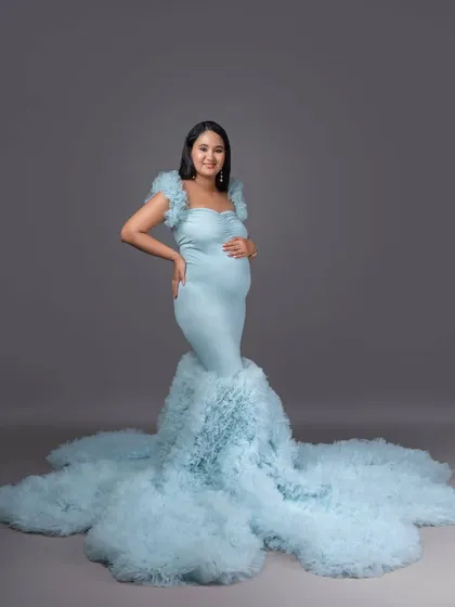 A simple, elegant portrait in a light blue mermaid-style gown against a clean grey background, emphasizing the beautiful silhouette.