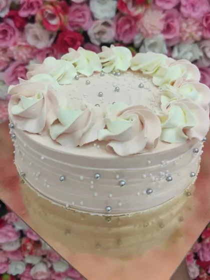 A customized Blueberry cake with a lovely pink hue. The sides are textured and dotted with silver pearls, while the top is decorated with delicate two-toned frosting rosettes.