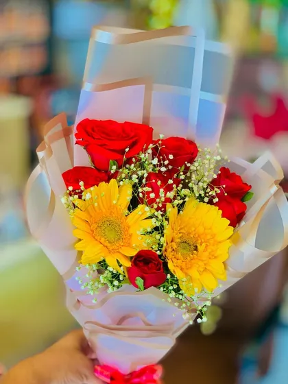 A charming small bouquet featuring yellow gerbera daisies and red roses. The simple wrapping and red ribbon make this a sweet and cheerful gift.