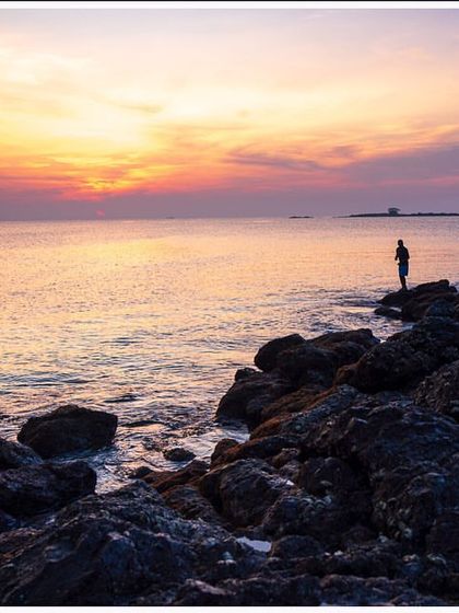 A lone figure stands on the rocks against a vibrant sunset in the Andaman Islands. This image captures a moment of solitude and connection with the vastness of the ocean.