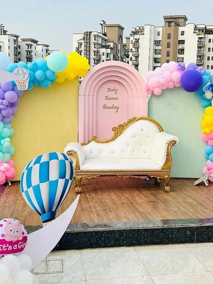 We create beautiful memories with our themed baby shower decorations, even on a rooftop. This setup includes a pastel color palette, a large crescent moon prop, hot air balloon models, and a comfortable lounge seat for the parents to be, all set against a city skyline.