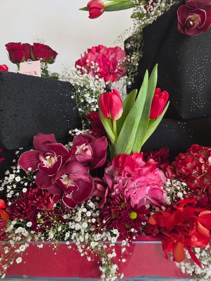 An intimate look at the rich textures within the arrangement, highlighting the deep burgundy orchids and bright red carnations.