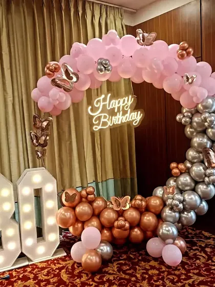 A grand 80th birthday celebration with a circular balloon arch in pink, rose gold, and silver. The design is highlighted by large, bright marquee numbers for the age and a 'Happy Birthday' neon sign, creating a perfect photo opportunity.