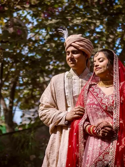 The couple takes a gentle stroll under the trees, bathed in dappled sunlight. This candid shot captures a quiet, reflective moment on their wedding day.