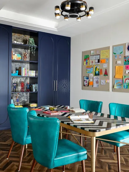 This kids' activity room features a large table with a chevron pattern, perfect for arts and crafts. The deep blue wardrobes have open shelving to display toys and creations, and a large corkboard shows off their artwork.