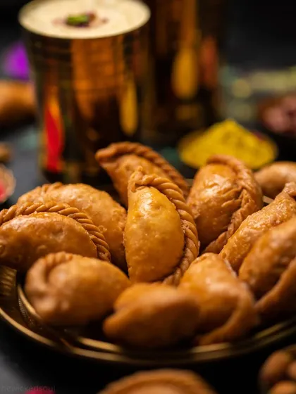 A close-up shot focusing on the plate of Gujjiya. The dark, moody lighting makes the golden-fried pastry stand out beautifully.