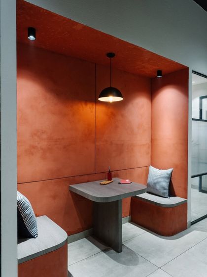 A close-up of the red-walled breakout nook, featuring built-in seating and a small table. The textured wall finish adds depth and warmth to the compact space.