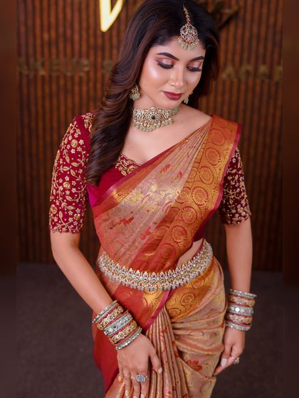 A model in a beige and red silk saree. This is a classic combination, and the drape is styled to look elegant and sophisticated for a reception or formal event.