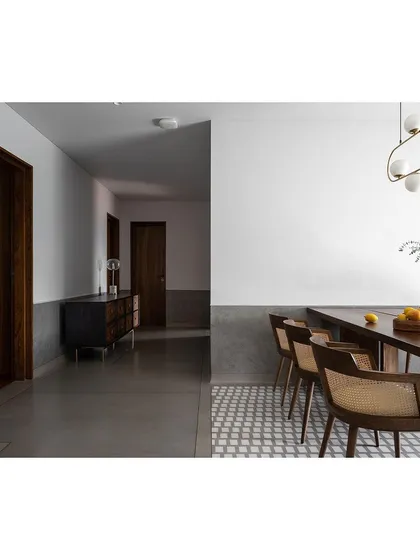 A clean and modern dining space where a patterned tile floor delineates the area, set against a corridor of polished grey concrete.