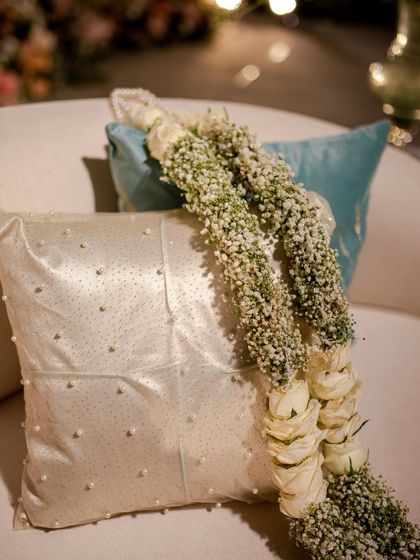 A beautiful varmala made of baby's breath and white roses, resting on a pearl-studded cushion.