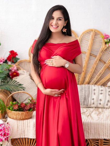 A joyful portrait of the mother-to-be in a vibrant red gown. Her bright smile and the warm, rustic tones of the boho set create an image that is full of life and happiness.