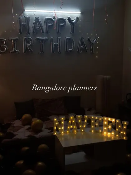 Sometimes, simple is the most romantic. A cozy bedroom birthday surprise with 'Happy Birthday' foil balloons and the name spelled out in warm marquee letters.