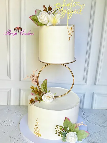An elegant floating engagement cake that creates a modern and sophisticated look. The two white tiers are separated by a golden ring and adorned with white roses and touches of gold leaf.