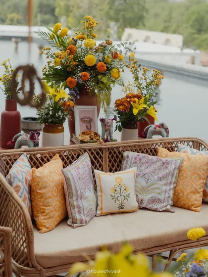 A beautiful shot of a rattan sofa with block-printed cushions, set against the backdrop of the pool and decorated with marigold arrangements.