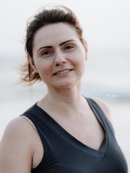 A classic headshot-style portrait taken outdoors with the ocean in the background. The clean, bright lighting is flattering and professional.