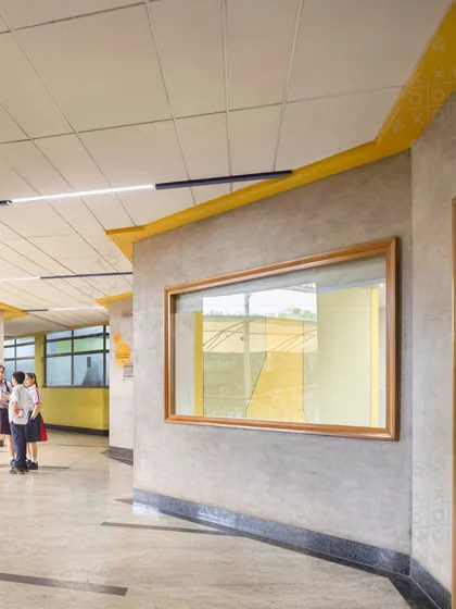 A corridor at GD Goenka Public School, Vasant Kunj, with a large window looking out onto the playground. The design connects the interior with the outdoors and uses color to enrich the students' daily experience.