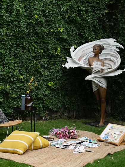 A dramatic sculpture of a woman wrapped in swirling fabric stands in a garden clearing. This piece acts as a powerful focal point, turning the lawn into an outdoor gallery space for art and inspiration.