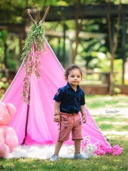 This toddler stands proudly in front of his pink teepee and teddy bear. The outdoor setting provides a beautiful, natural backdrop for this themed photoshoot.